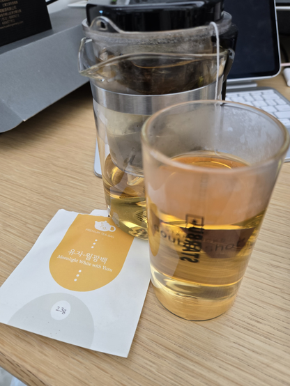 유리잔 뒤쪽으로 표일배가 있다. 둘 다 차가 담겨있다. 잔 밑에는 티백 봉투가 있다.